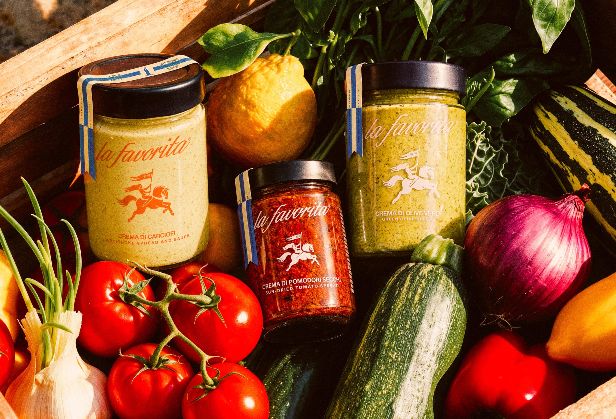 Barattoli La Favorita di crema di carciofi, pomodori secchi e olive verdi in una cassetta di verdure fresche