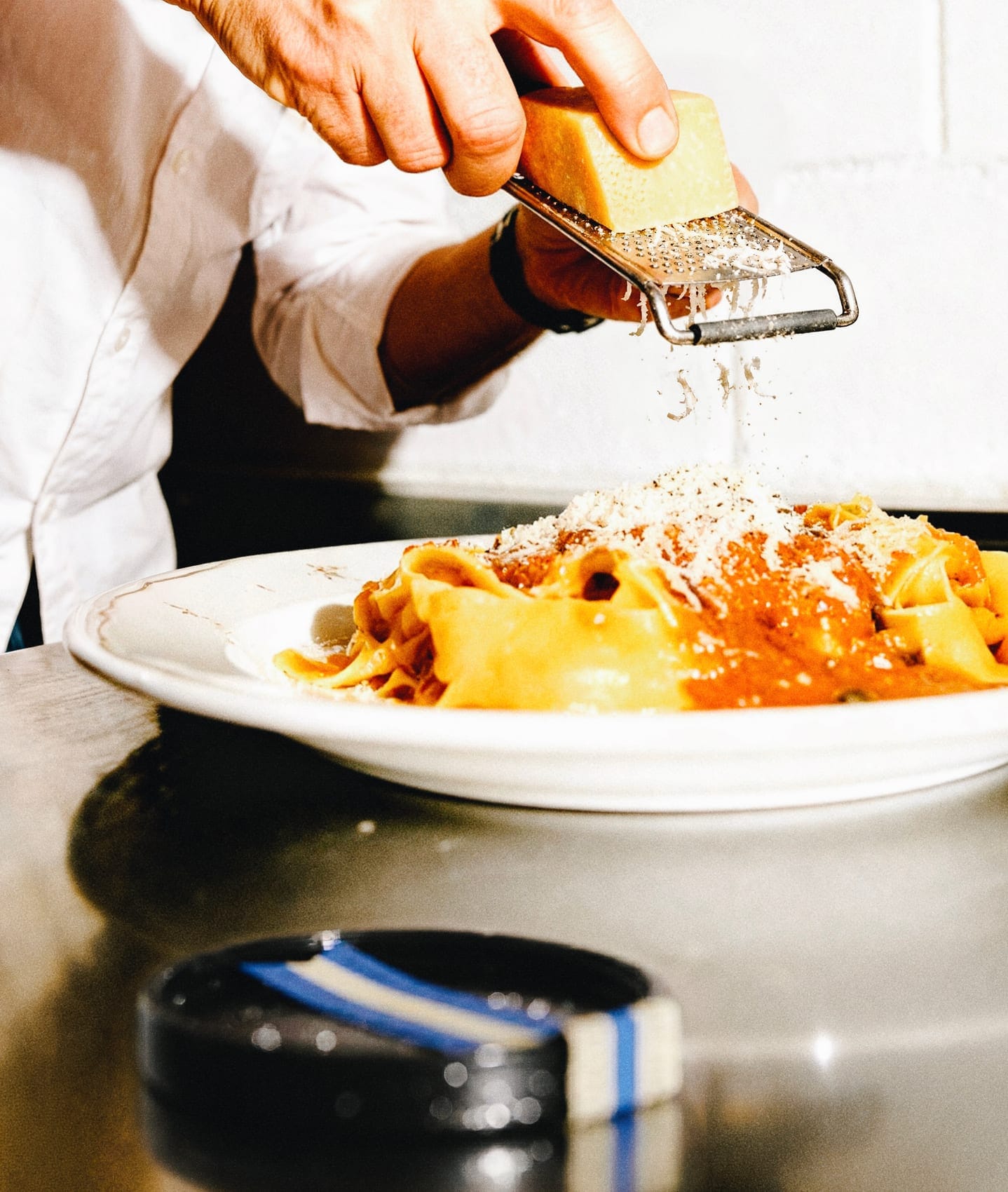 Uno chef grattugia il formaggio su un piatto di pappardelle al sugo